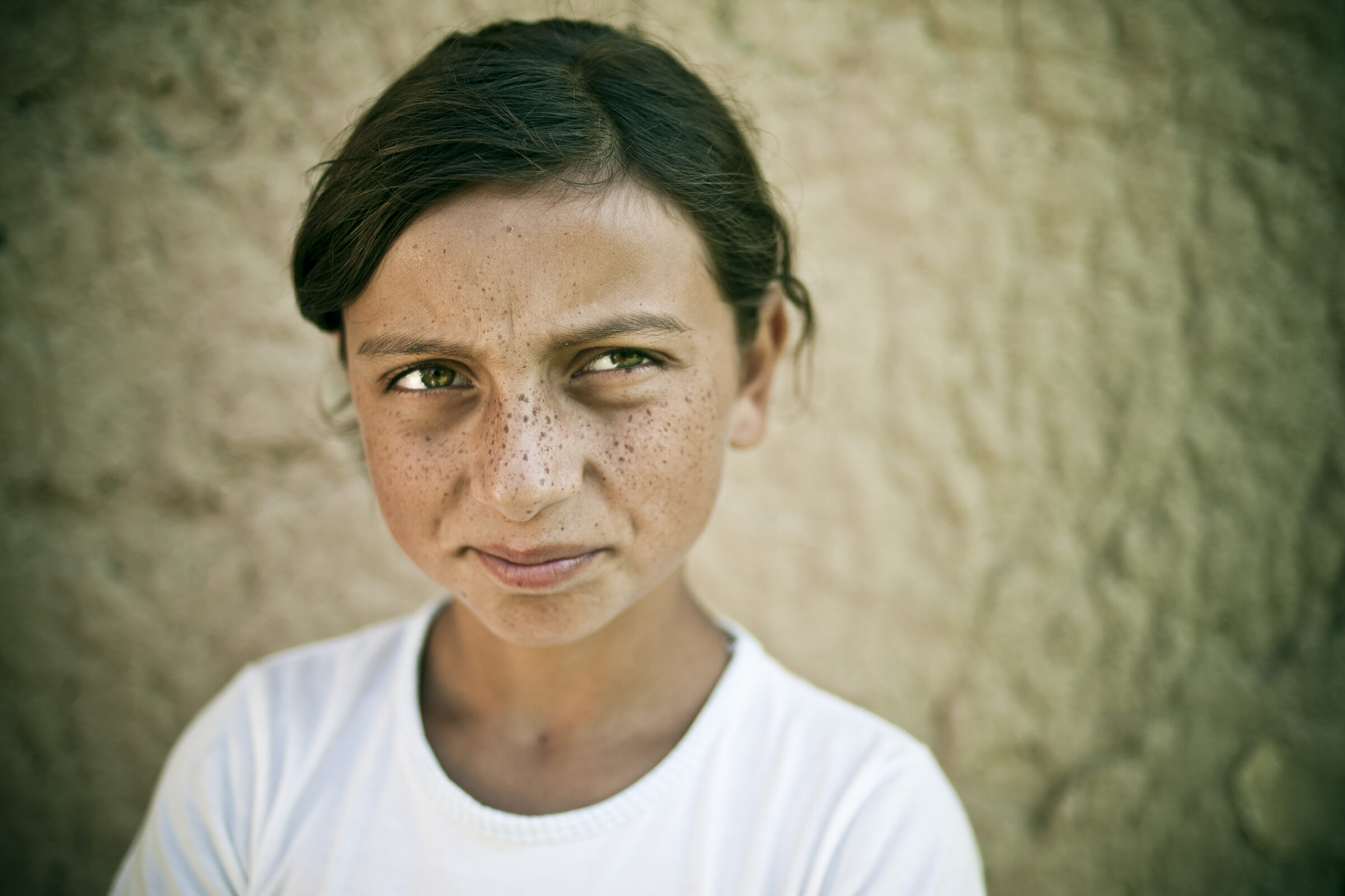 Close portrait of a freckled girl against a stone wall