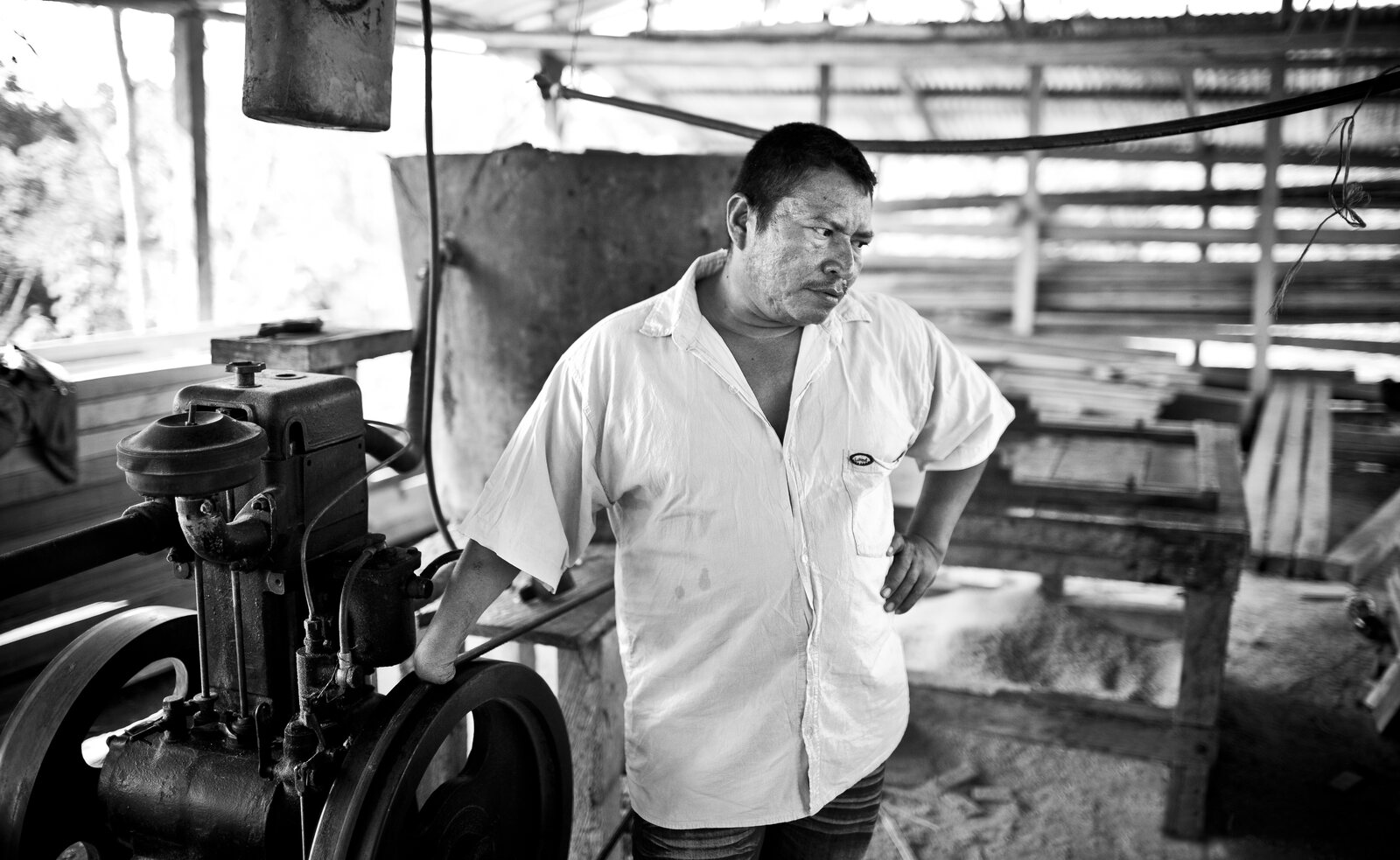 A man standing thoughtfully beside a large machine in a rustic workshop