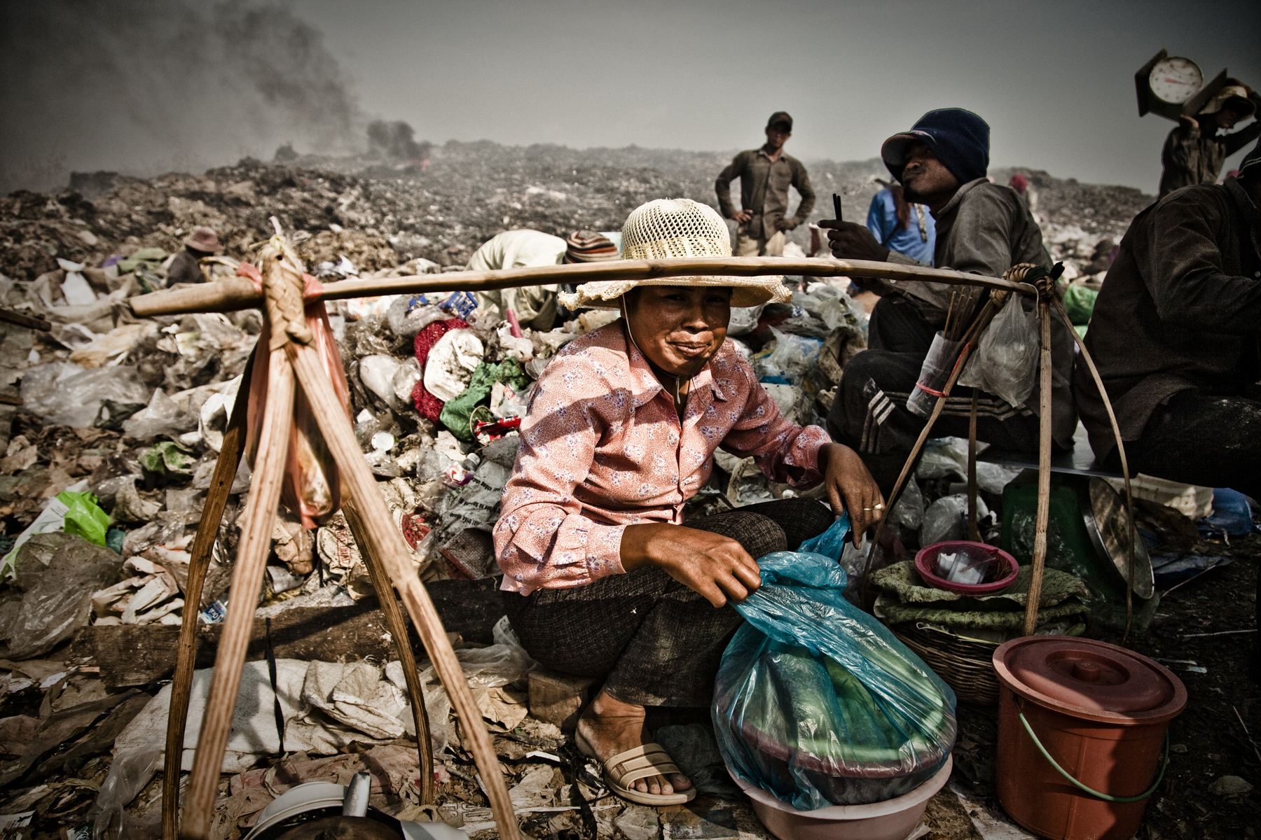 Workers carrying loads across a landfill at dawn