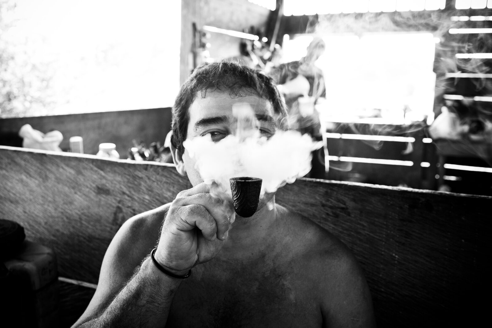A man exhaling a thick plume of pipe smoke that veils his face