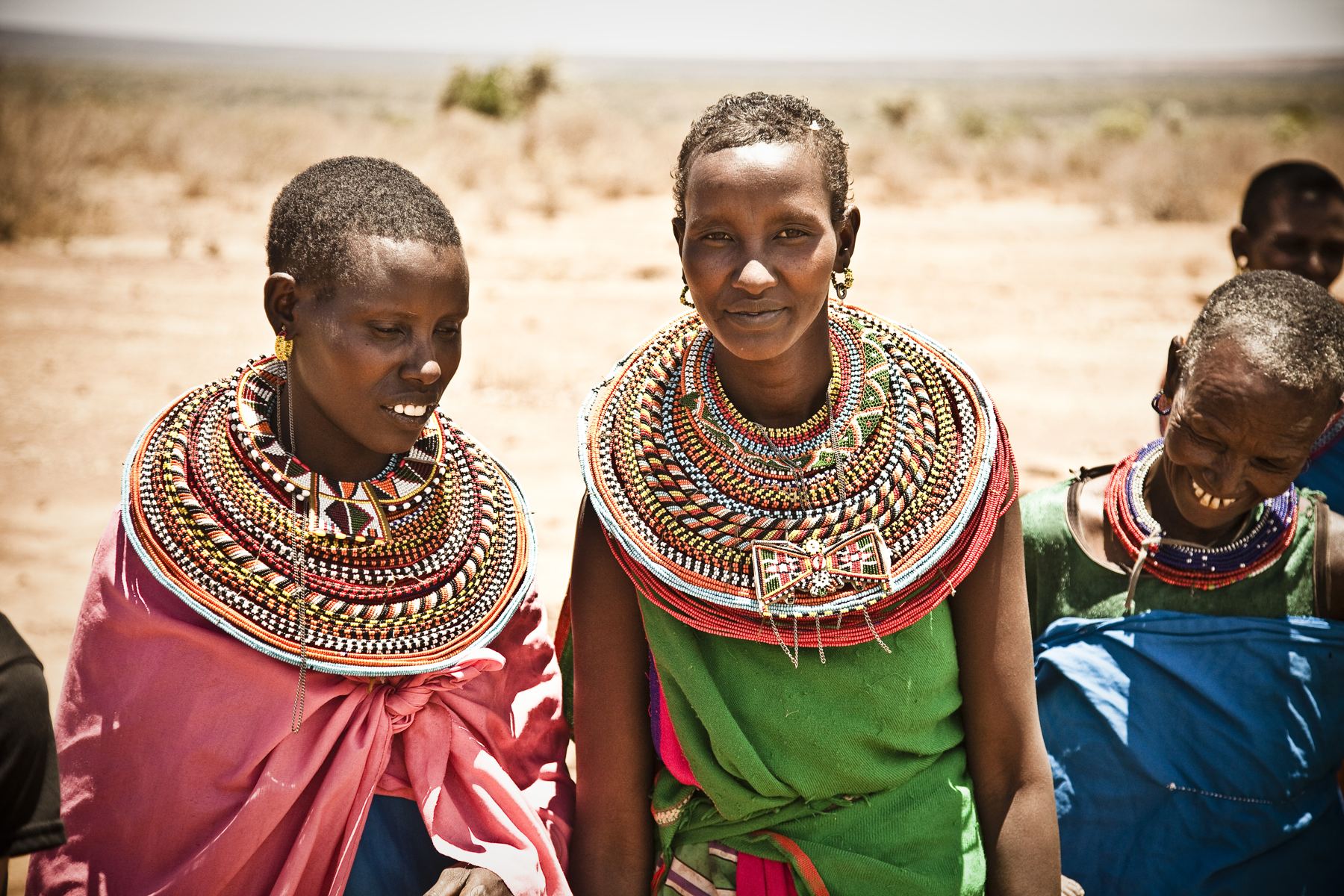 A woman in a patterned headscarf smiling outside her home